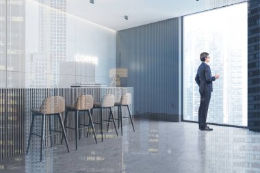 Beyaz ve gri duvarları, beton zemini ve tabureli gri bar tezgahı olan şık bir kahve dükkanında duran genç işadamı. Renkli resim çift pozlama