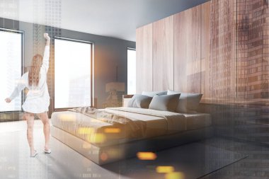 Modern yatak odasında gri ve ahşap duvarları, beton zeminde halısı ve rahat kral yatağı olan pijamalı genç bir kadın. Renkli bulanık resim çift pozlama