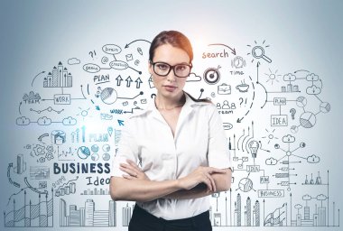 Üzerinde yaratıcı iş planı çizimi olan gri duvarın yanında çapraz kollu duran genç ve güzel bir iş kadını. Liderlik ve başarı kavramı