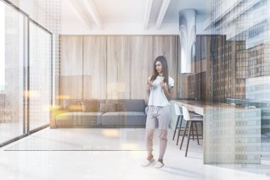 Kahveli ve akıllı telefonlu genç bir kadın modern mutfakta tahta duvarları, gri tezgahları, tabureleri ve balkona yakın rahat gri kanepesi olan bir bar. Renkli resim çift pozlama