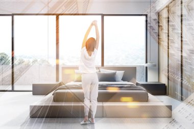 Beyaz ve ahşap duvarları, kral boyutunda yatağı ve güzel manzaralı balkonu olan şık, güneşli bir yatak odasında duran genç bir kadının arka görüntüsü. Renkli resim çift pozlama