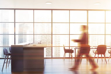 Panoramik mutfakta ahşap zemin, tabureli gri ve mavi bar ve sandalyeli yemek masası ile yürüyen bulanık genç adam. Tonu ayarlanmış resim