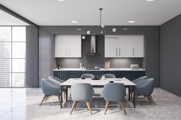 Interior of panoramic kitchen with gray walls, tiled floor, dark blue countertops and white cupboards. Dining table with blue chairs in the center. 3d rendering