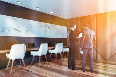 Gri ve beyaz mermer duvarları, ahşap zeminleri ve dizüstü bilgisayarları ve sıra sıra sandalyeleri olan lüks bir ofis ortamında dokümanları tartışan iki işadamı. Tonu ayarlanmış resim