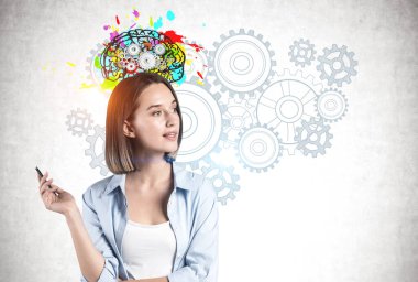 Düşünceli, gündelik kıyafetlerle genç bir kadın beton duvarın yanında dikiliyor. Üzerinde vitesler çizilmiş renkli bir beyni var. Beyin fırtınası ve yaratıcılık kavramı.