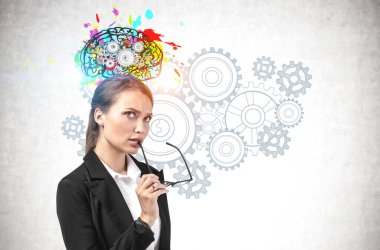 Üzerinde vitesler çizilmiş renkli beyin çizimi olan beton duvarın yanında duran düşünceli genç bir iş kadını. Beyin fırtınası, yaratıcılık ve eğitim kavramı