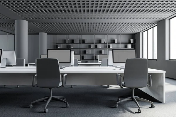 Open space office of consulting company with grey walls, carpeted floor, rows of white computer tables and bookcase with folders in background. 3d rendering