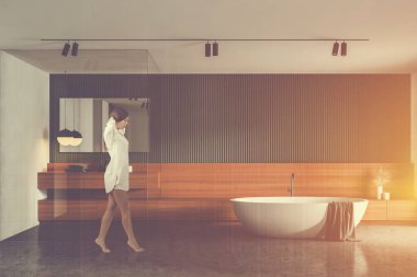 Geniş banyoda yeşil ve beyaz duvarları, beton zemini, rahat küveti ve aynalı yuvarlak lavabosu olan gecelikli genç bir kadın. Rahatlama kavramı. Renkli resim çift pozlama