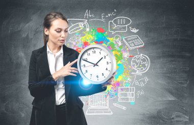 Ciddi genç bir iş kadını elinde büyük bir saat tutarak üzerinde yaratıcı eğitim skeci çizilmiş bir karatahtanın yanında duruyor. Eğitim ve kariyer kavramı