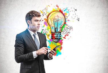 Üzerinde yaratıcı ve parlak bir iş fikri çizimi olan beton duvarın yanında duran akıllı telefonlu yakışıklı genç bir işadamı. Başlangıcın konsepti