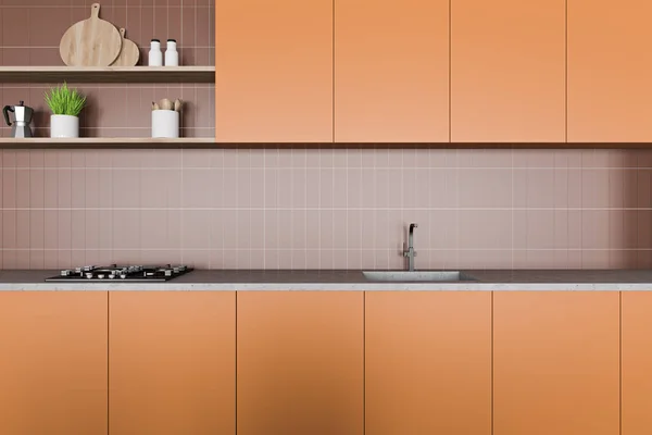 Interior of stylish kitchen with brown tile walls, orange cupboards and countertops with built in sink and cooker. Shelves with dishes and cutting boards. 3d rendering