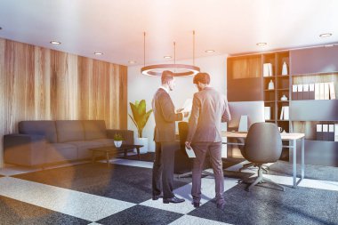 Lüks Ceo ofisinde, beyaz ve ahşap duvarları, bilgisayar masası, kitaplığı ve kanepesi olan belgeleri tartışan iki genç iş adamı. Liderlik kavramı. Tonu ayarlanmış resim