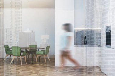 Geniş bir mutfakta beyaz duvarları, tahta zemini, beyaz tezgahları ve yeşil sandalyeli yuvarlak yemek masası olan bulanık genç bir kadın. Renkli resim çift pozlama