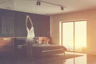 Lüks yatak odasında, yeşil beyaz duvarları, beton zemini ve rahat kral yatağı olan pijamalı genç bir kadın. Renkli resim çift pozlama