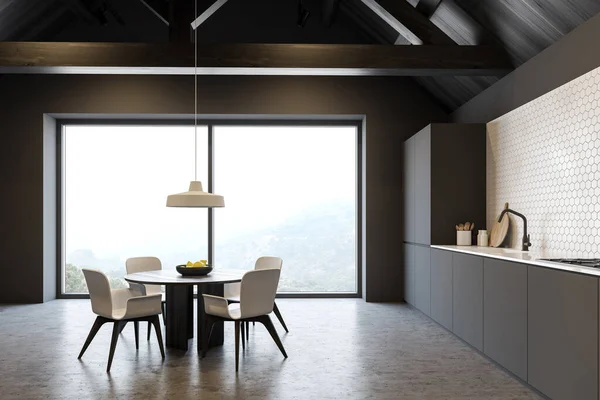 Interior of spacious attic mansion kitchen with grey and white tiled walls, concrete floor, gray countertops and round dining table with chairs. Window with blurry view. 3d rendering