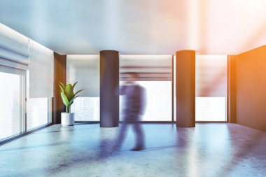 Bulanık genç işadamı gri duvarları, sütunları, beton zemini ve panoramik pencereleriyle boş ofis odasında yürüyor. Gayrimenkul kavramı. Tonu ayarlanmış resim