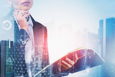 Bulanık internet arayüzü ve yüksek teknoloji ikonları ile soyut bir şehirde elinde defterle tanınmayan genç bir iş kadını. Teknoloji kavramı. Tonu ayarlanmış resim