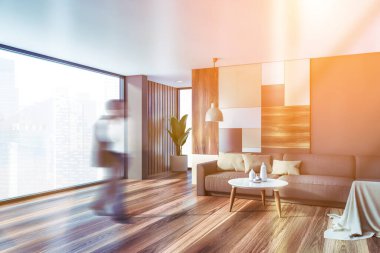 Gri ve parlak geometrik desenli duvarları, ahşap zemini ve sehpanın yanındaki rahat gri koltuğu olan şık oturma odasında yürüyen takım elbiseli bulanık Afrikalı Amerikalı bir adam. Tonu ayarlanmış resim