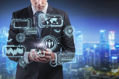 Bulanık gece şehrinde fütüristik iş arayüzü ile birlikte akıllı telefon kullanan tanınmayan bir iş adamı. Yüksek teknoloji ve akıllı şehir kavramı. Tonu ayarlanmış resim