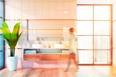 Pembe fayans duvarları, ahşap zemini ve yatay aynası olan tezgahta rahat bir çift lavabo olan lüks banyoda yürüyen bulanık bir genç kadın. Tonu ayarlanmış resim