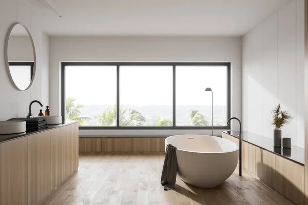酒店浴室内部有白色和木制墙壁 木制地板 舒适的白色浴缸和圆形镜子水池 有模糊的热带景色的窗户 3D渲染 — 图库照片