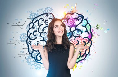 Üzerinde parlak yaratıcı ve analitik beyin çizimi olan gri duvarın yanında duran dalgalı siyah saçlı neşeli Avrupalı genç bir kadın. Beyin fırtınası ve bilim kavramı