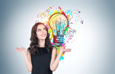 Siyah elbiseli neşeli genç Avrupalı kadın gri duvara çizilmiş parlak iş fikri çizimini gösteriyor. Beyin fırtınası ve yaratıcılık kavramı