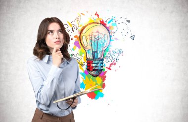 Not defteri ve dalgalı siyah saçlı düşünceli genç bir kadın renkli iş fikri çizimiyle beton duvarın yanında duruyor. İş eğitimi kavramı