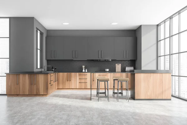 Interior of modern kitchen with gray and brick walls, concrete floor, wooden countertops with built in sink and cooker and grey cupboards. Wooden bar with stools. 3d rendering