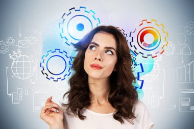 Üzerinde yaratıcı iş planı çizimi ve renkli vitesler olan gri duvarın yanında duran dalgalı uzun saçlı düşünceli genç iş kadınının portresi. Beyin fırtınası ve strateji kavramı