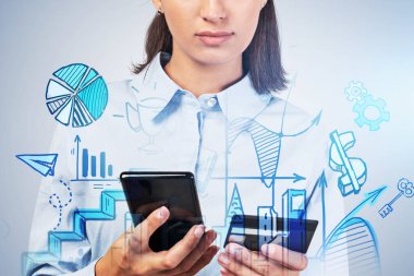 Akıllı telefonu ve kredi kartı olan Avrupalı genç bir iş kadınının portresi gri duvarın yanında duruyor ve mavi online alışveriş skecini iki kez gösteriyor. E- ticaret anlayışı. Tonu ayarlanmış resim