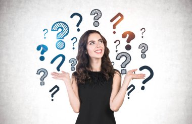 Siyah elbiseli, dalgalı uzun saçlı neşeli genç kadın beton duvarın yanında soru işaretleriyle seçim yapıyor..