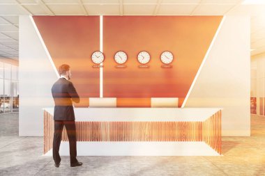 Beyaz ve kahverengi duvarları, resepsiyon masası ve saatleri dünya başkentlerini gösteren saatleriyle modern uluslararası şirket ofisindeki kendine güvenen işadamının dikiz görüntüsü. Tonu ayarlanmış resim