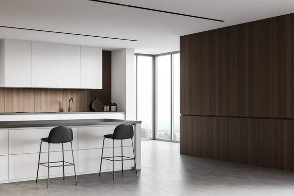 Corner of modern kitchen with white and wooden walls, concrete floor, white cupboards and countertops with built in appliances and comfortable bar with stools. Window with blurry view. 3d rendering