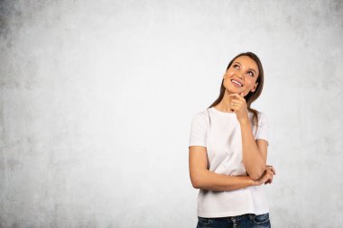 Yukarı bakan, uzun sarı saçlı, sıradan elbiseli genç Avrupalı bir kadının portresi. Planlama kavramı ve iyi fikir. Beton duvar arka planı. Model