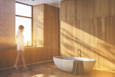 Beyaz ve ahşap duvarları, ahşap zemini, rahat küveti ve pencerenin yanında lavabosu olan güneşli banyoda yürüyen bulanık genç bir kadın. Renkli resim çift pozlama