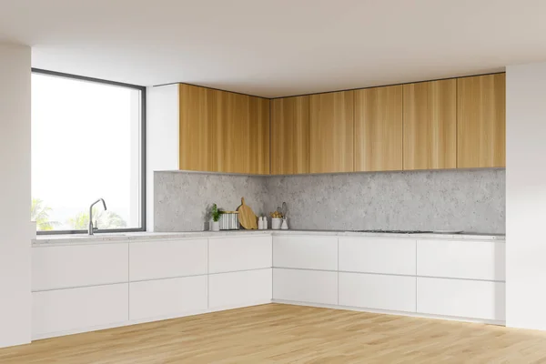 Corner of comfortable kitchen with white walls, wooden floor, white countertops with built in sink and cooker and wooden cupboards. Window with blurry tropical view. 3d rendering