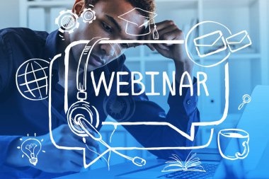 Bilgisayarlı ciddi bir Afro-Amerikalı adamın portresi. Bulanık odada notlar alıyor. Yaratıcı Webinar skecini iki kez gösteriyor. Tonu ayarlanmış resim