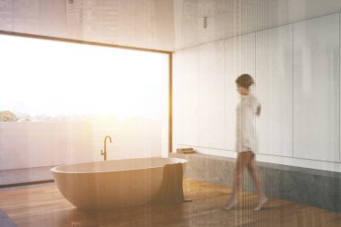 Beyaz duvarları, ahşap zemini, rahat küveti ve büyük balkonu olan geniş güneşli banyoda yürüyen bulanık genç bir kadın. Renkli resim çift pozlama