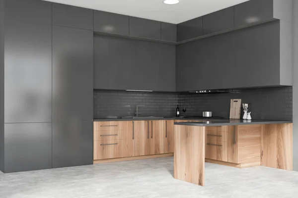 Corner of stylish kitchen with grey walls, concrete floor, wooden countertops with built in sink and cooker, grey cupboards and island. 3d rendering