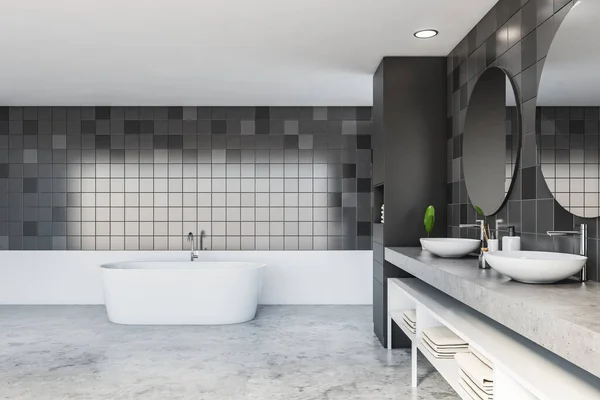 Interior of stylish bathroom with grey tiled and white walls, concrete floor, comfortable double sink with round mirrors, bathtub and white shelves with towels. 3d rendering