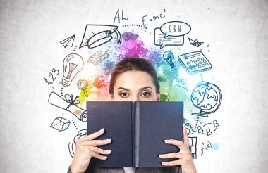 Yüzünü siyah kitapla kaplayan güzel genç bir kadın üzerine renkli bir çizim çizilmiş beton duvarın yanında duruyor. Bilgi ve kariyer seçimi kavramı