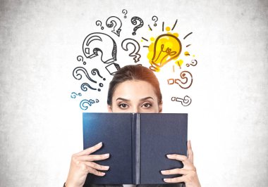 Üzerinde soru işaretleri ve ampuller olan beton duvarın yanında duran yüzünü siyah kitapla kaplayan güzel bir genç kadının portresi. Eğitim kavramı, seçim ve iyi fikir