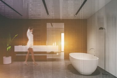 Beyaz ve ahşap duvarları, beton zemini, rahat küveti ve büyük aynası olan güneşli banyoda yürüyen bulanık bir genç kadın. Renkli resim çift pozlama