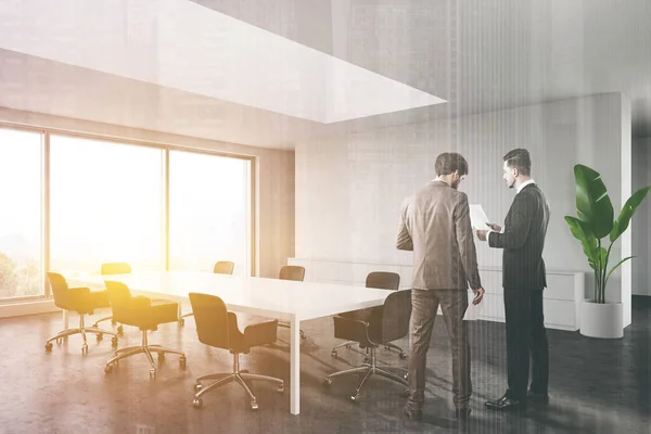 Two managers discussing business in stylish sunlit meeting room with white walls, long conference table and black chairs. Blurry mountain view. Toned image double exposure