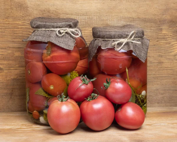 jars with canned tomatoes and fresh tomatoes on wooden background