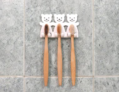 Üç bambu diş fırçasından oluşan bir aile seti diş fırçası tutacağındaki banyo duvarında asılı. Ekolojik yaşam tarzı.