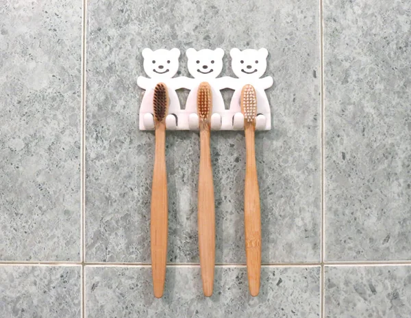 A family set of three bamboo toothbrushes hang on the bathrooms wall in toothbrush holder. Ecological lifestyle. 스톡 사진