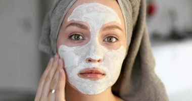 Yüzüne beyaz nemlendirici maske takan saçlarında havlu olan bir kızın portresi.