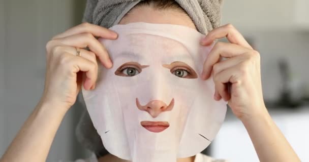 Jong meisje met handdoek op haren aanbrengen cosmetische vel masker op gezicht, vooraanzicht. — Stockvideo